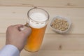 Male hand holding a mug of draft beer. Peanuts in the bowl on the table. Royalty Free Stock Photo