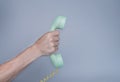 Male hand holding an old blue plastic telephone receiver on gray background. Close up remote handset from a retro rotary Royalty Free Stock Photo