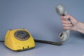 Male hand holding an old plastic telephone receiver near yellow rotary telephone on gray background. Close up remote Royalty Free Stock Photo