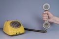 Male hand holding an old plastic telephone receiver near yellow rotary telephone on gray background. Close up remote Royalty Free Stock Photo