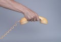 Male hand holding an old yellow plastic telephone receiver on gray background. Close up remote handset from a retro Royalty Free Stock Photo