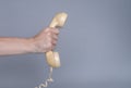 Male hand holding an old yellow plastic telephone receiver on gray background. Close up remote handset from a retro Royalty Free Stock Photo