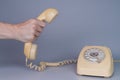 Male hand holding an old yellow plastic telephone receiver near rotary telephone on gray background. Close up remote Royalty Free Stock Photo