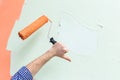 Male hand holding paint roller dipped in orange colour and showing thumb down against green wall. Copy space.