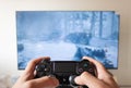 A male hand holding a play station 4 controller with first person video game in a smart tv at background