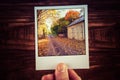 Male hand holding polaroid photo of rural road passing wooden sh