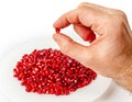 Male hand holding pomegranate seed on background of white bowl with red pomegranate seeds