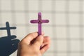 Male hand holding purple wooden cross with shadow. Christianity, faith, holy week and lent season.