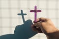 Male hand holding purple wooden cross with shadow. Christianity, faith, holy week and lent season.