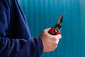 Male hand holding red close gardening scissors. Side view. Gardener with pruning shears in hand. Close up of a male hand