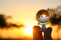 male hand holding small crystal globe in front of sunset Royalty Free Stock Photo