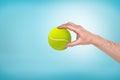 Male hand holding small tennis ball between fingers on blue background Royalty Free Stock Photo