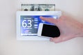 Male hand holding smart phone to operate heating or cooling via digital touch screen thermostat for home energy savings Royalty Free Stock Photo