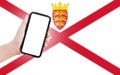 Male hand holding smartphone with blank on screen, on background of blurred flag of Jersey. Close-up view.