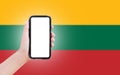 Male hand holding smartphone with blank on screen, on background of blurred flag of Lithuania. Close-up view.