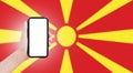 Male hand holding smartphone with blank on screen, on background of blurred flag of North Macedonia. Close-up view.