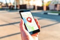 Male hand holding holding smartphone with online-a map on which the geolocation icon. In the background, a blurred street. Close Royalty Free Stock Photo