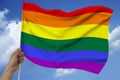 Male hand holds against the background of the sky with clouds the rainbow multi-colored flag of the LGBT community on a luxurious