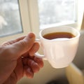 Male hand holds cup of tea in front of window. Soft focus moving action photo.