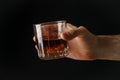 Male hand holds glass of whiskey on black background