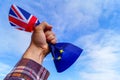 A male hand holds in his fist the flags of England and the European Union against a blue sky and symbolizes Brexit or No Brexit