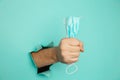 A male hand holds a medical mask through a hole in a blue wall. Medical breakthrough concept