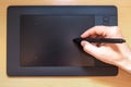 Male hand holds a pen on a black graphics tablet on a written wooden table