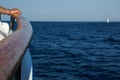 A male hand holds on to a wooden rail of a boat out at sea in th