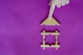 Male hand installs the roof on toy children wooden house on lilac background