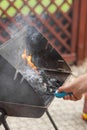 Male hand kindles fire in grill with long blue lighter. Man using BBQ lighter to start fire for charcoal in brazier.