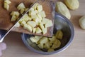 Male hand with knife sweeps raw diced potatoes into metal bowl from cutting board