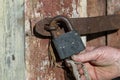 Male hand of an old man closes a rusty padlock on a wooden door, closeup. Vintage background Royalty Free Stock Photo