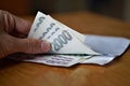 Male hand opening a white envelope full of Czech currency (Czech Crowns, CZK, Kc) on the wooden table as a symbol of cash transfer