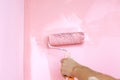 A male hand paints a wall with a paint roller in pink