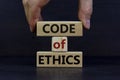 Male hand placing a block with word `code` on blocks tower with words `code of ethics`. Beautiful dark wooden background. Copy Royalty Free Stock Photo