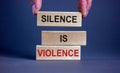 Male hand placing a block with word `silence` on top of a blocks tower with words `silence is violence`. Beautiful grey backgr Royalty Free Stock Photo