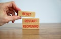 Male hand placing a blocks with word `reset` on top of a blocks tower wiyh words `restart, reopening`. Wooden table. Beautiful