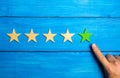 The male hand points to the fifth green star on a blue wooden background. Five Stars. Rating of restaurant or hotel, application. Royalty Free Stock Photo