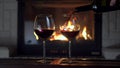 Male hand pouring red wine from bottle into two glass goblet flame of fireplace in background