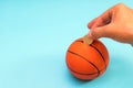 Male hand putting coin into the piggy bank with a shape of basket ball isolated on blue background Royalty Free Stock Photo