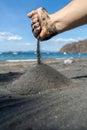 Male Hand releases black sand at the beach.