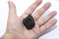 Male hand with a small piece of coal on a light background. Royalty Free Stock Photo