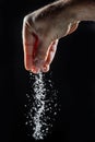 Male hand sprinkling edible salt at black background