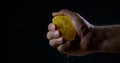 Male hand is squeezing a half of ripe orange, close-ip on black background Royalty Free Stock Photo