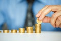 Male hand stacking gold coins into increasing columns