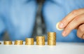 Male hand stacking gold coins into increasing columns