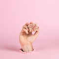 A male hand sticks out of a hole in paper on a pink background, holds a craft gift. Christmas concept, print blank, copy space