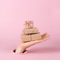 A male hand sticks out of a hole in paper on a pink background, holds a mountain of craft gifts. Christmas concept, print blank,