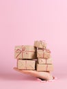 A male hand sticks out of a hole in paper on a pink background, holds a mountain of craft gifts. Christmas concept, print blank,