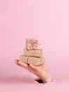 A male hand sticks out of a hole in paper on a pink background, holds a mountain of craft gifts. Christmas concept, print blank,